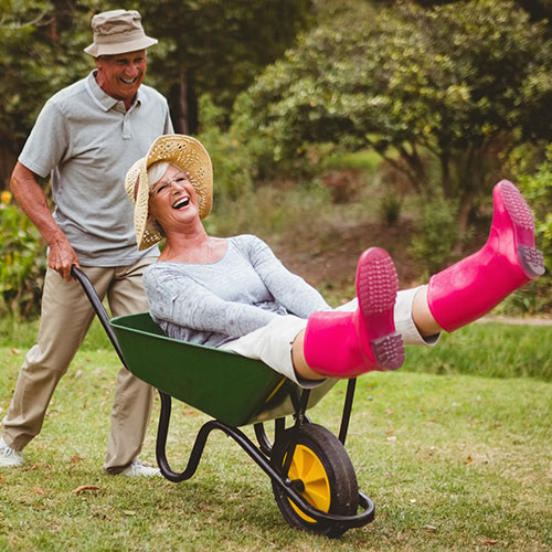 Older man pushing his smiling wife in garden wheelbarrow